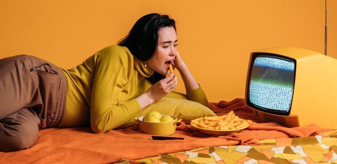 Eine Frau isst Fast Food vor dem Fernseher.