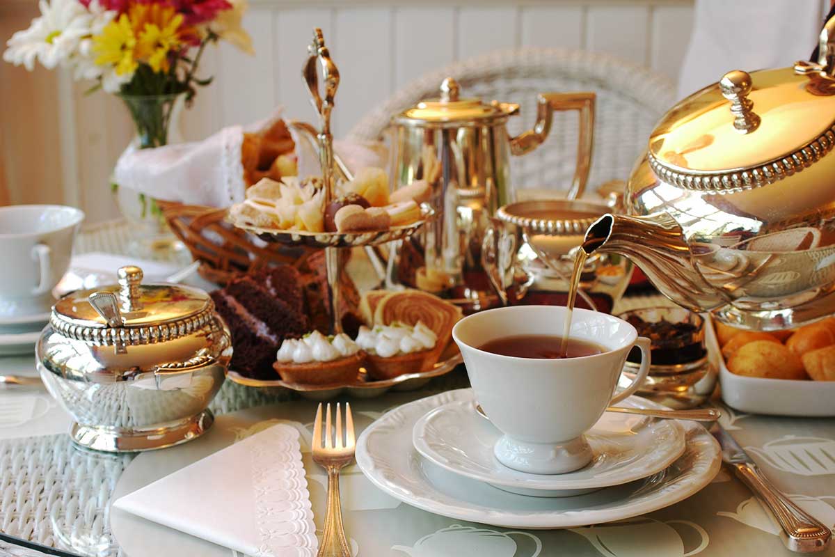 Ein typisches English Tea-Setting mit Tee-Krug und Etagere und Blumen auf dem Tisch.