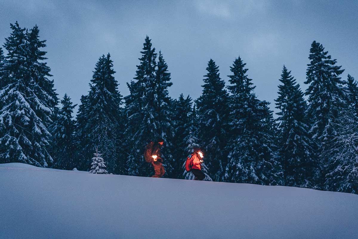 Zwei Personen sind am Nachtwandern mit einer Fackel im Schnee.