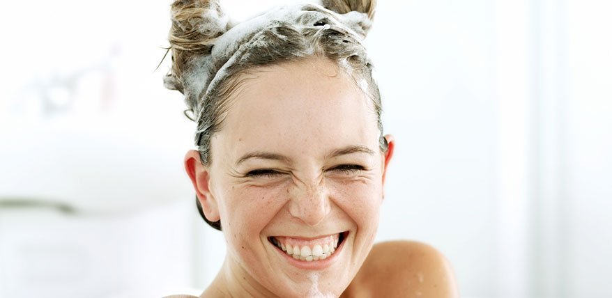 Lachende Frau mit einshampoonierten Haaren.