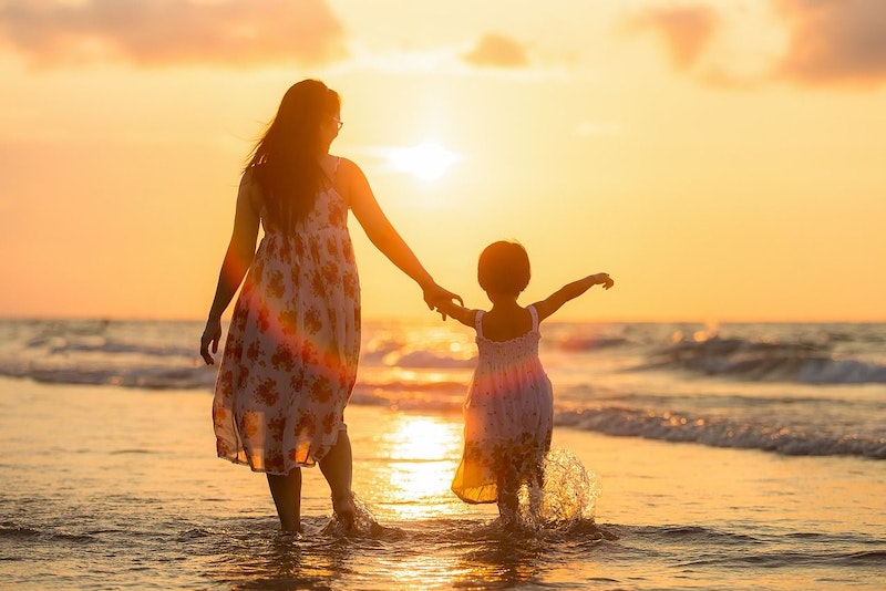 Eine Frau hält ihr Kind an der Hand im Sonnenuntergang am Meer.