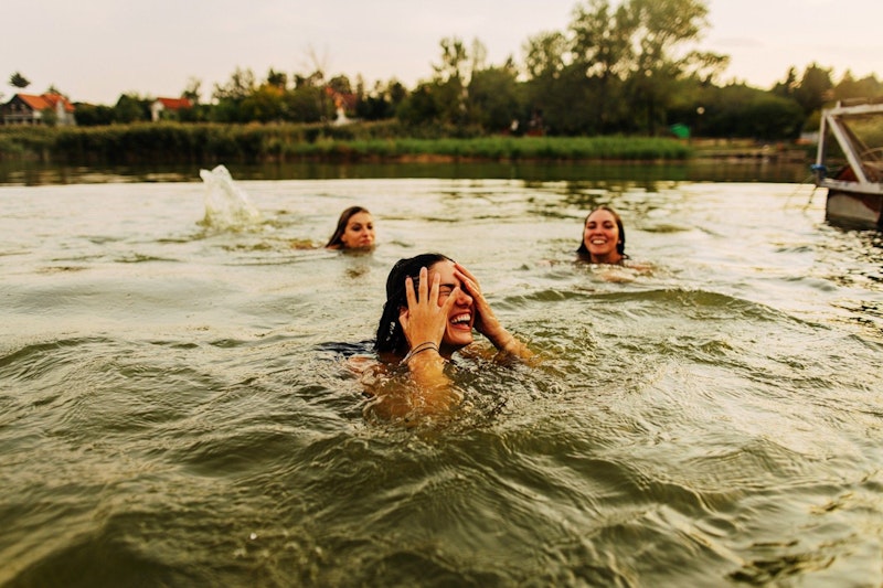 Foto von lächelnden Freundinnen, die in einem See schwimmen