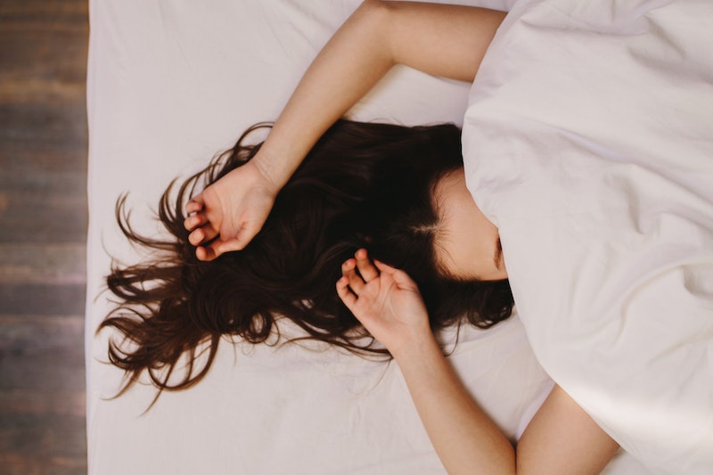 Frau liegt im Bett und versteckt ihr Gesicht unter der Decke. Zu sehen sind nur die Haare und die Arme.