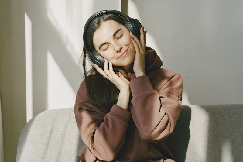 Eine junge Frau sitzt mit Kopfhörern auf dem Sofa. Sie hat die Augen geschlossen und lächelt.