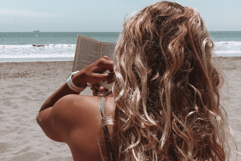 Eine Frau mit blonden Locken liest am Strand.