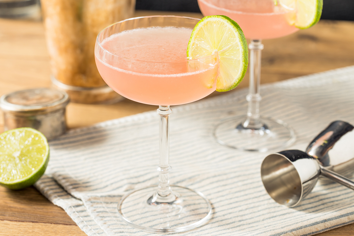 Ein rosa Cocktail mit Limette, Cosmopolitan, steht auf einem Tisch neben einem Shaker.
