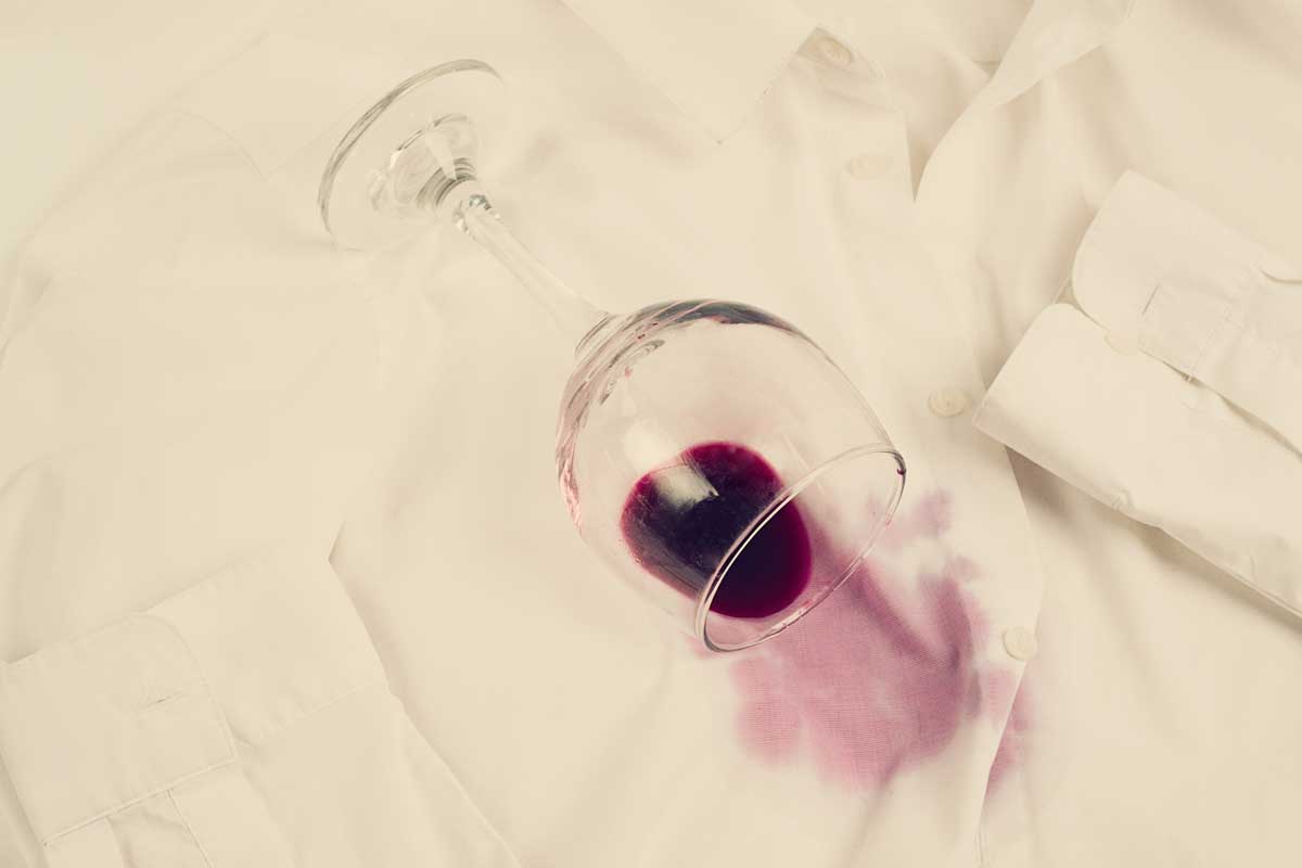 Ein Rotweinglas leert auf einem weissen Hemd aus und verursacht Flecken.