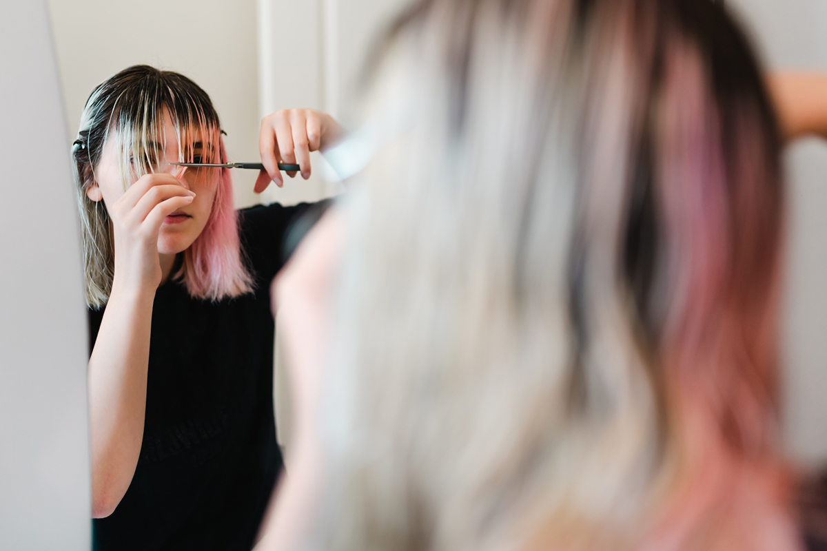 Eine junge Frau schneidet sich die Haare vor dem Spiegel selbst.
