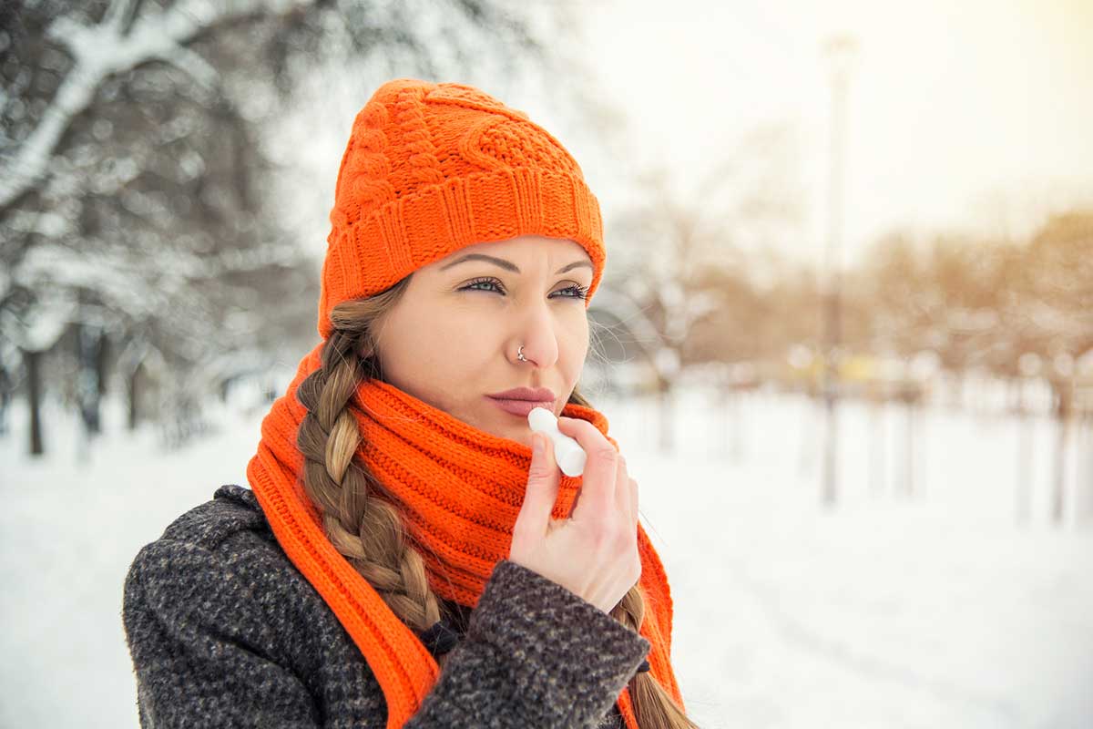 Eine Frau steht im Schnee und pflegt ihre Lippen.