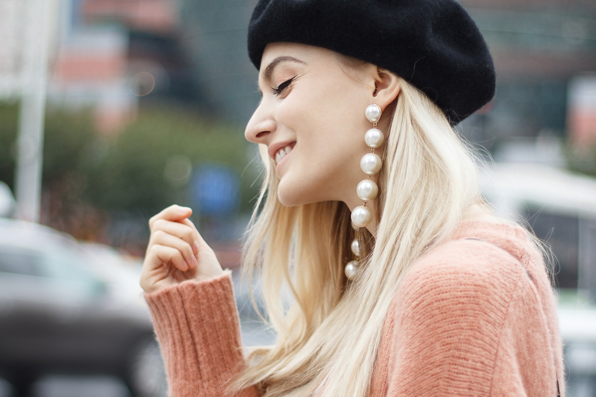 Eine junge, blonde Frau trägt grosse Perlohrringe ganz im Ohrring-Trend 2023.