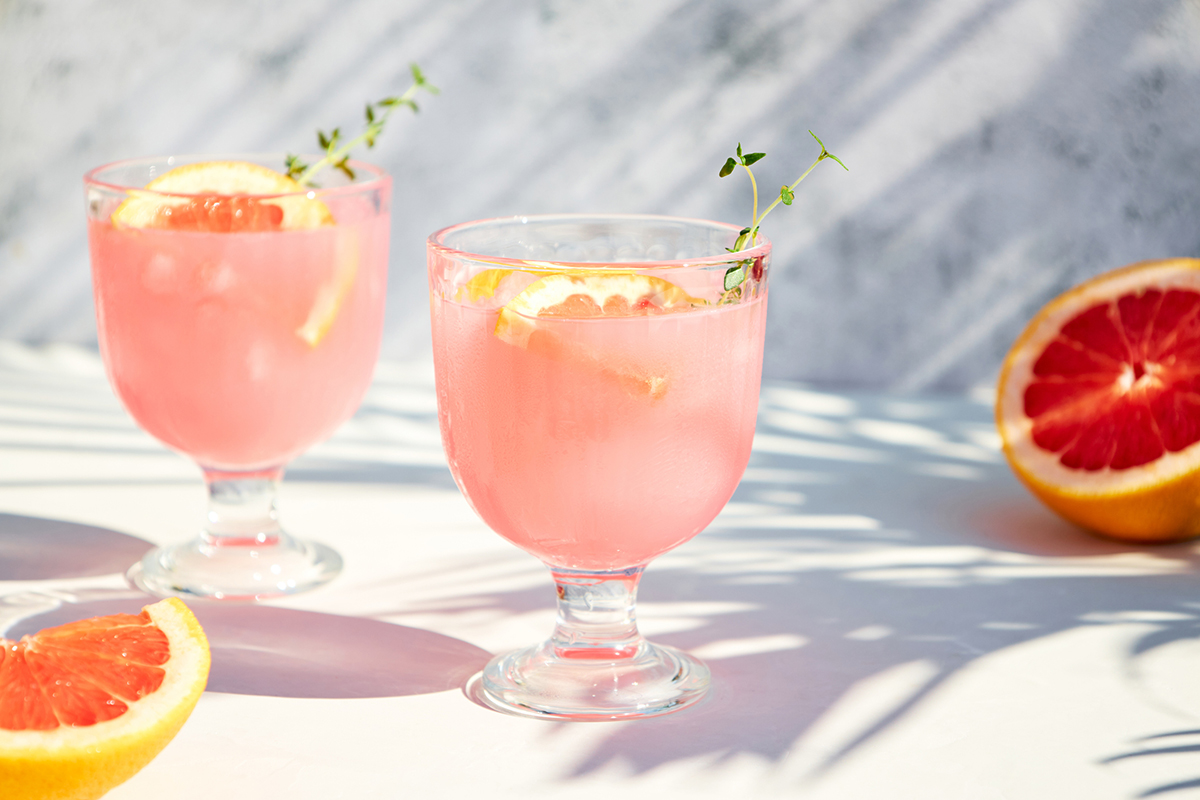 Cocktail mit Grapefruit, Paloma, auf einem Tisch mit dem Schattenwurf von Palmblättern.